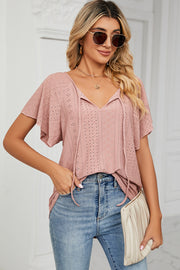 Pink eyelet tie-neck blouse with flutter sleeves and a V-neckline.