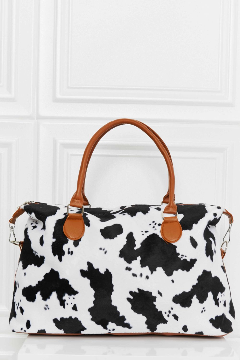 Satchel bag with cow print, brown leatherette handles and trim.