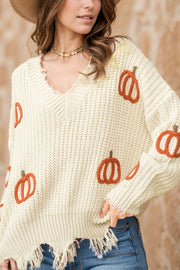 Beige distressed knit sweater with pumpkin embroidery, V-neck, and frayed hem.