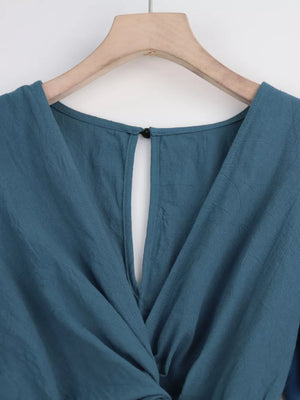 Haze Blue cotton romper with V-neck, button closure, and tie waist detail.