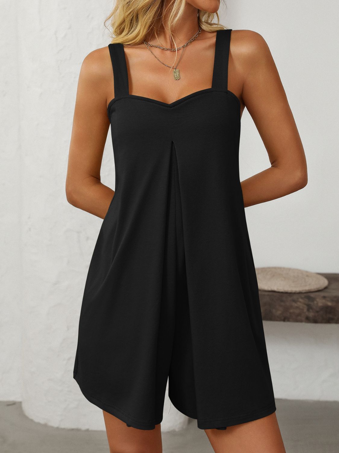 Black pleated bodice romper with sweetheart neckline and wide straps, featuring side pockets.