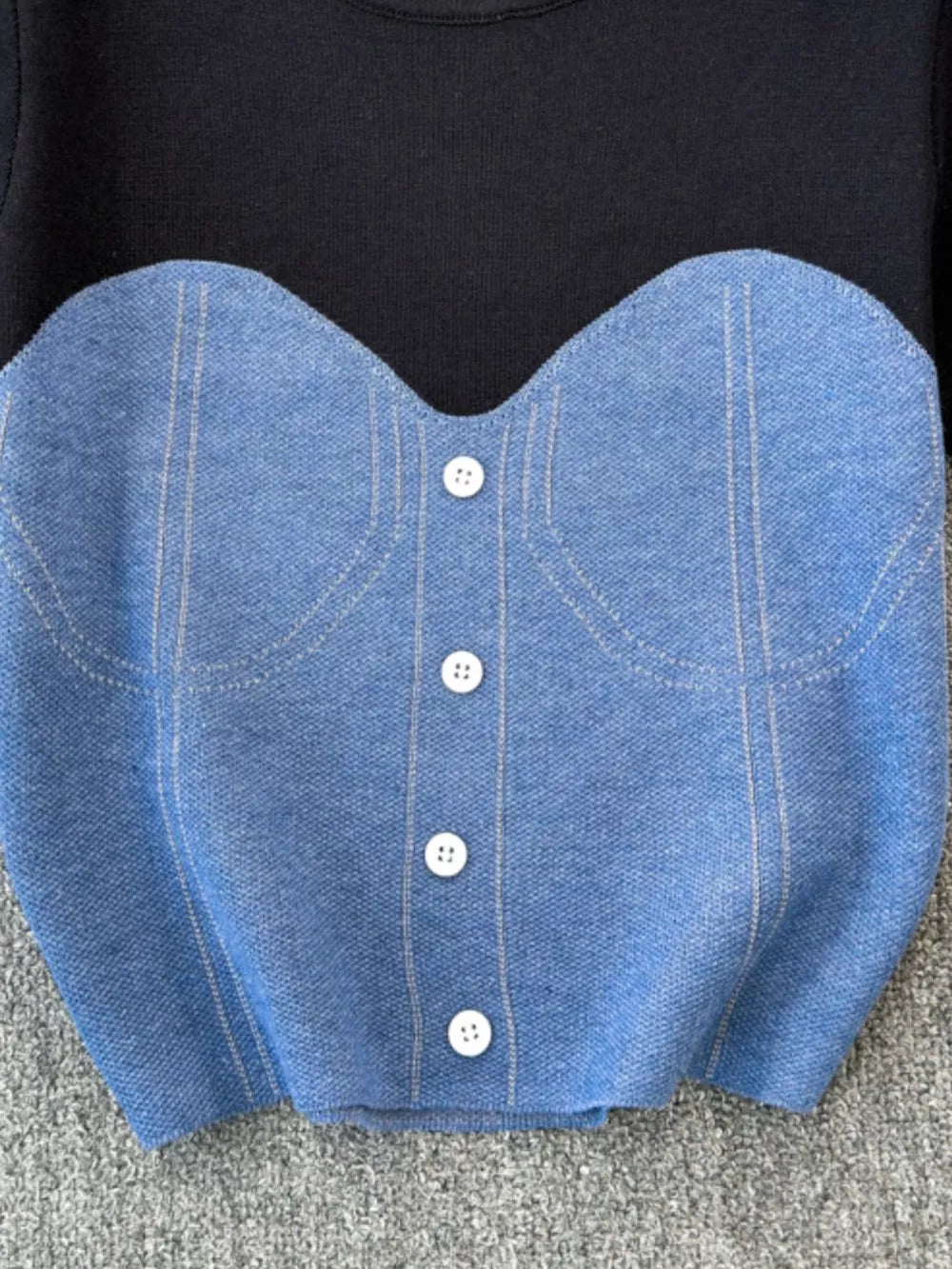 Color block knit t-shirt in black with a blue ribbed bustier detail and white buttons.