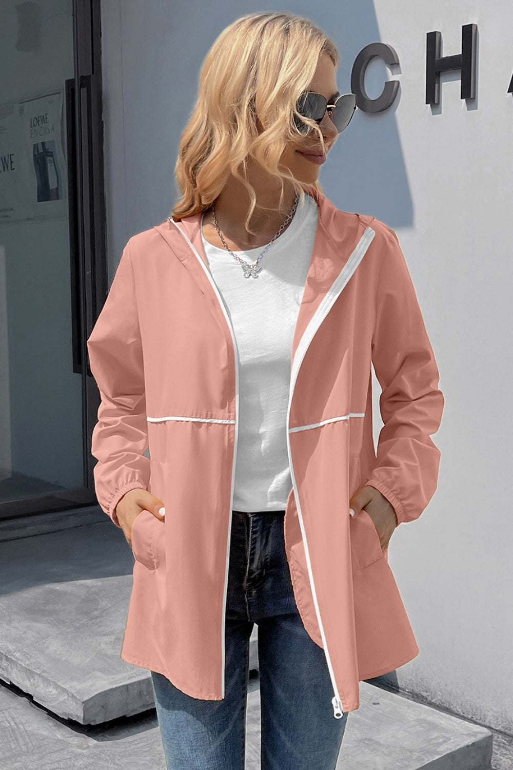Blush pink hooded rain coat with white trim and zipper, worn open over a white tee.
