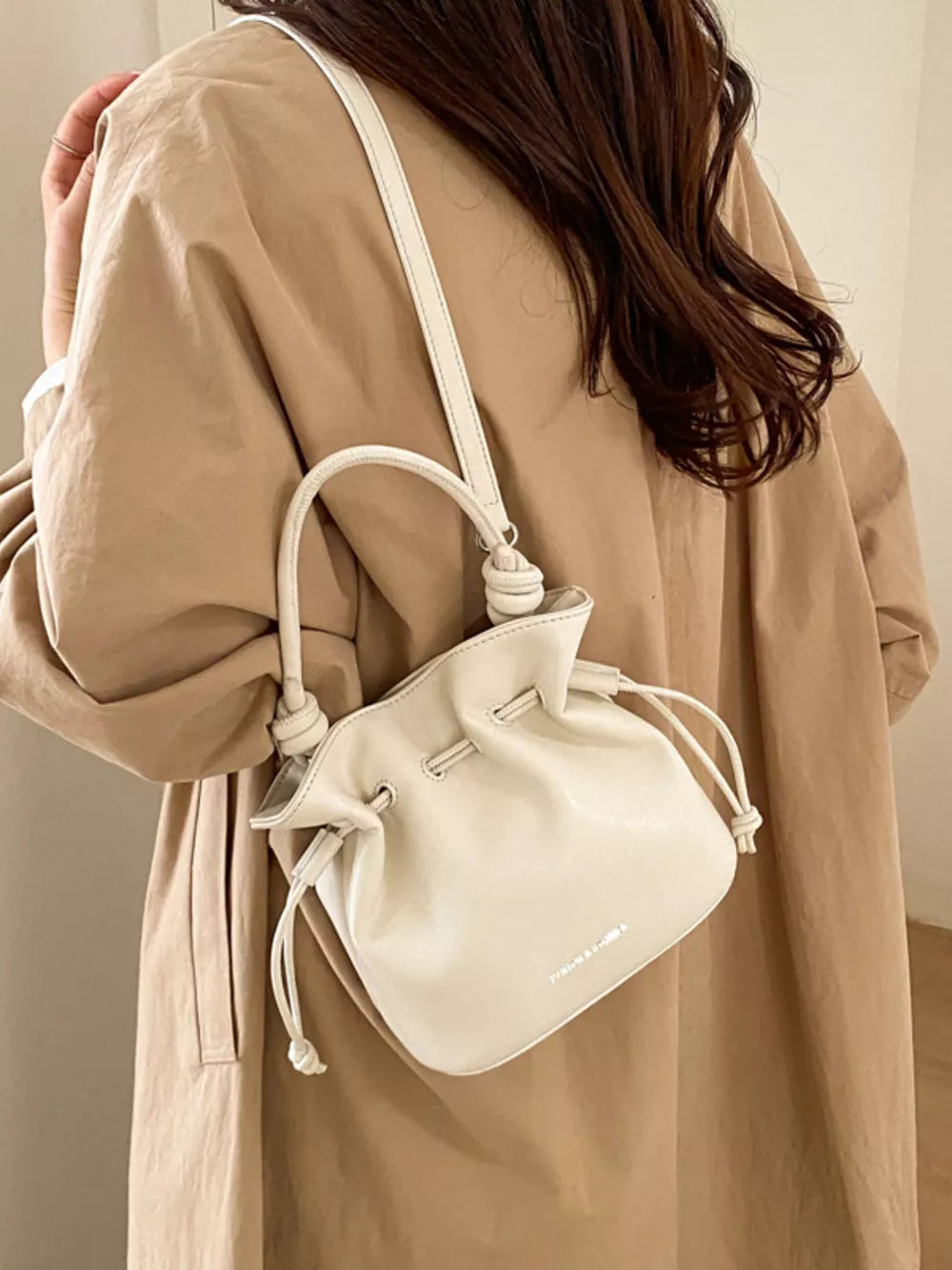 White pu leather cinch-top crossbody bag with knotted strap detail.