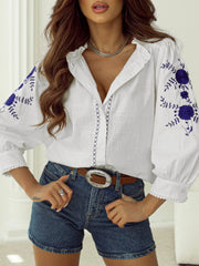 White linen blouse with blue floral embroidery and scalloped trim.