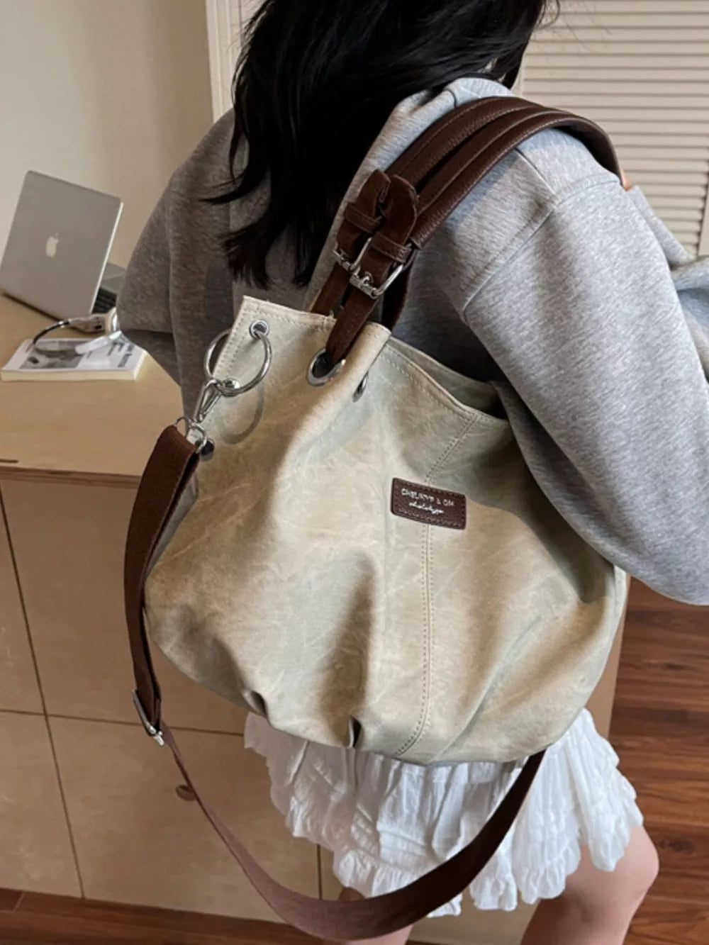 Slouchy crossbody bag in off-white canvas-like material with brown leather straps and adjustable buckle detail.