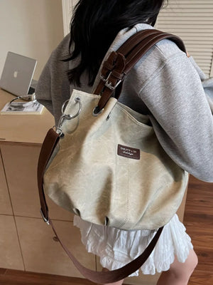 Slouchy crossbody bag in off-white canvas-like material with brown leather straps and adjustable buckle detail.