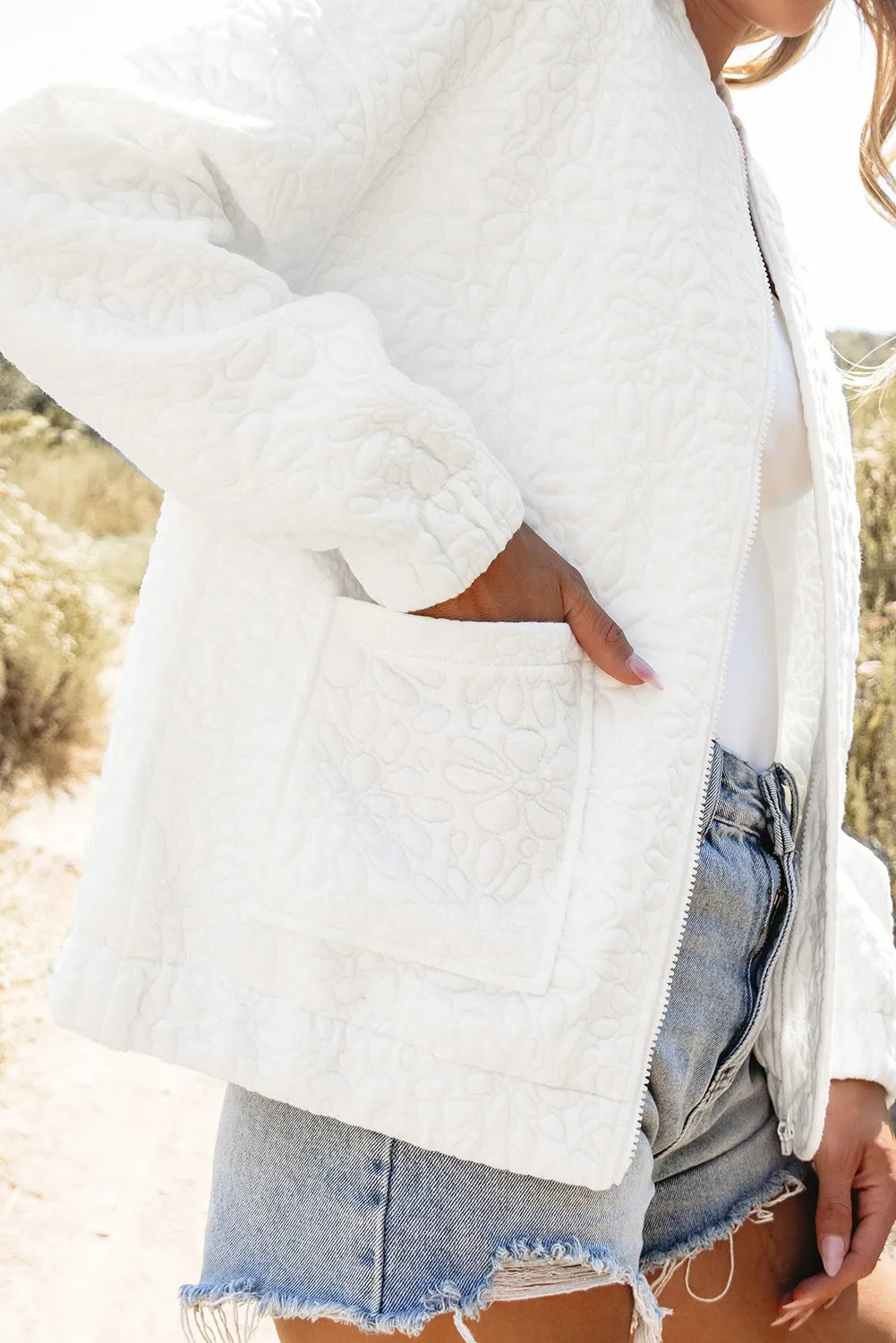 White quilted bomber jacket with floral pattern and chest pocket, worn with denim shorts.