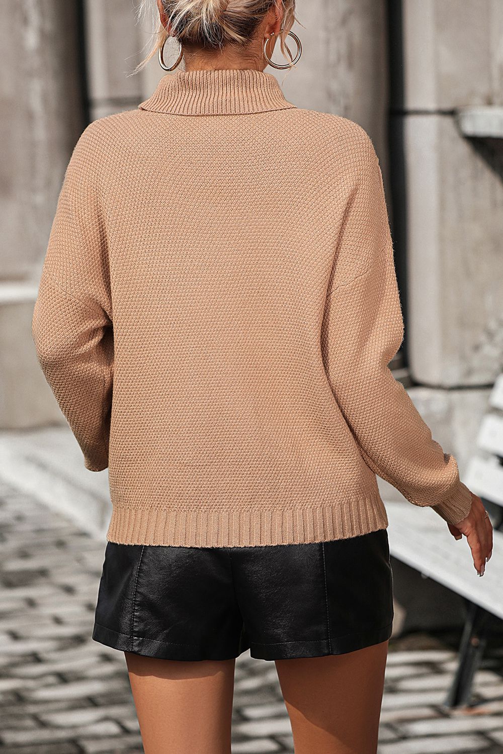 Beige turtleneck sweater with textured knit and ribbed cuffs, styled with black shorts.