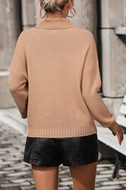 Beige turtleneck sweater with textured knit and ribbed cuffs, styled with black shorts.
