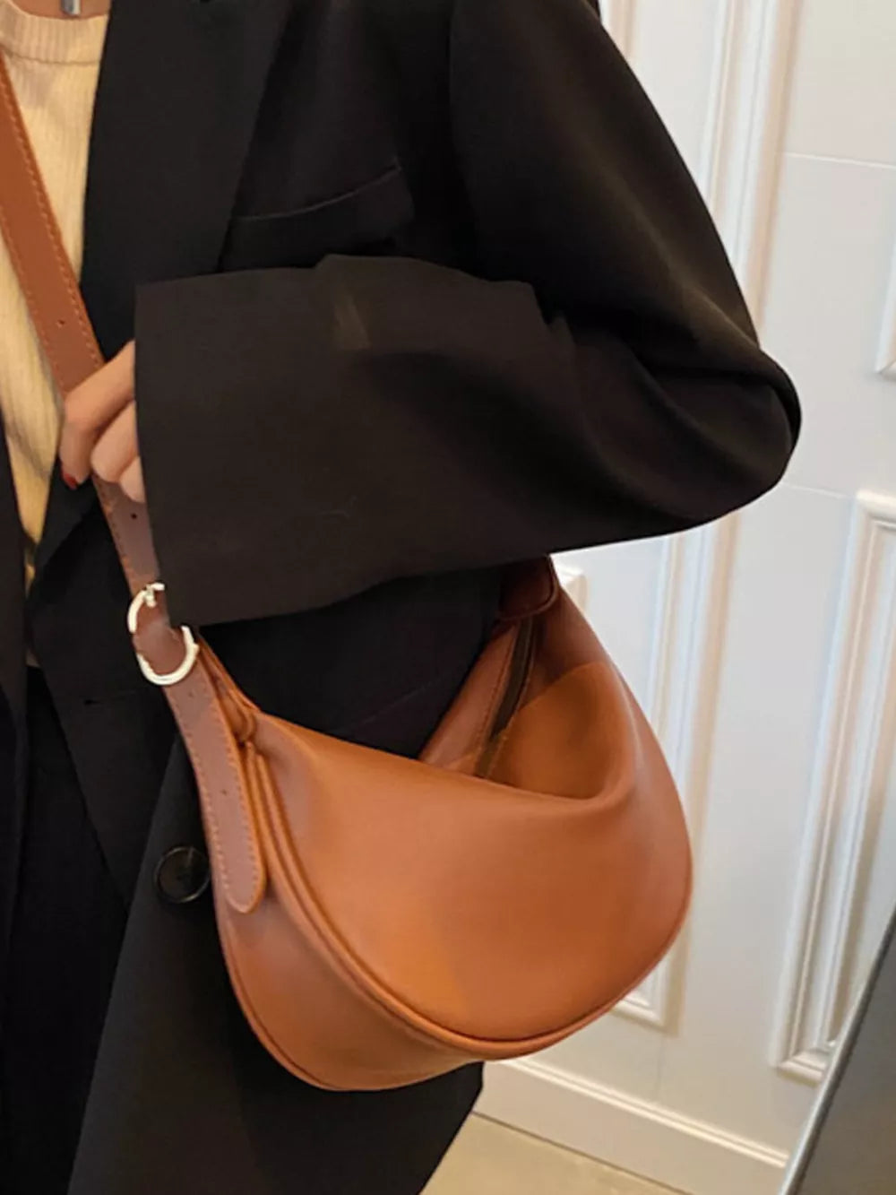 Brown crescent crossbody bag with adjustable strap and gold buckle detail.