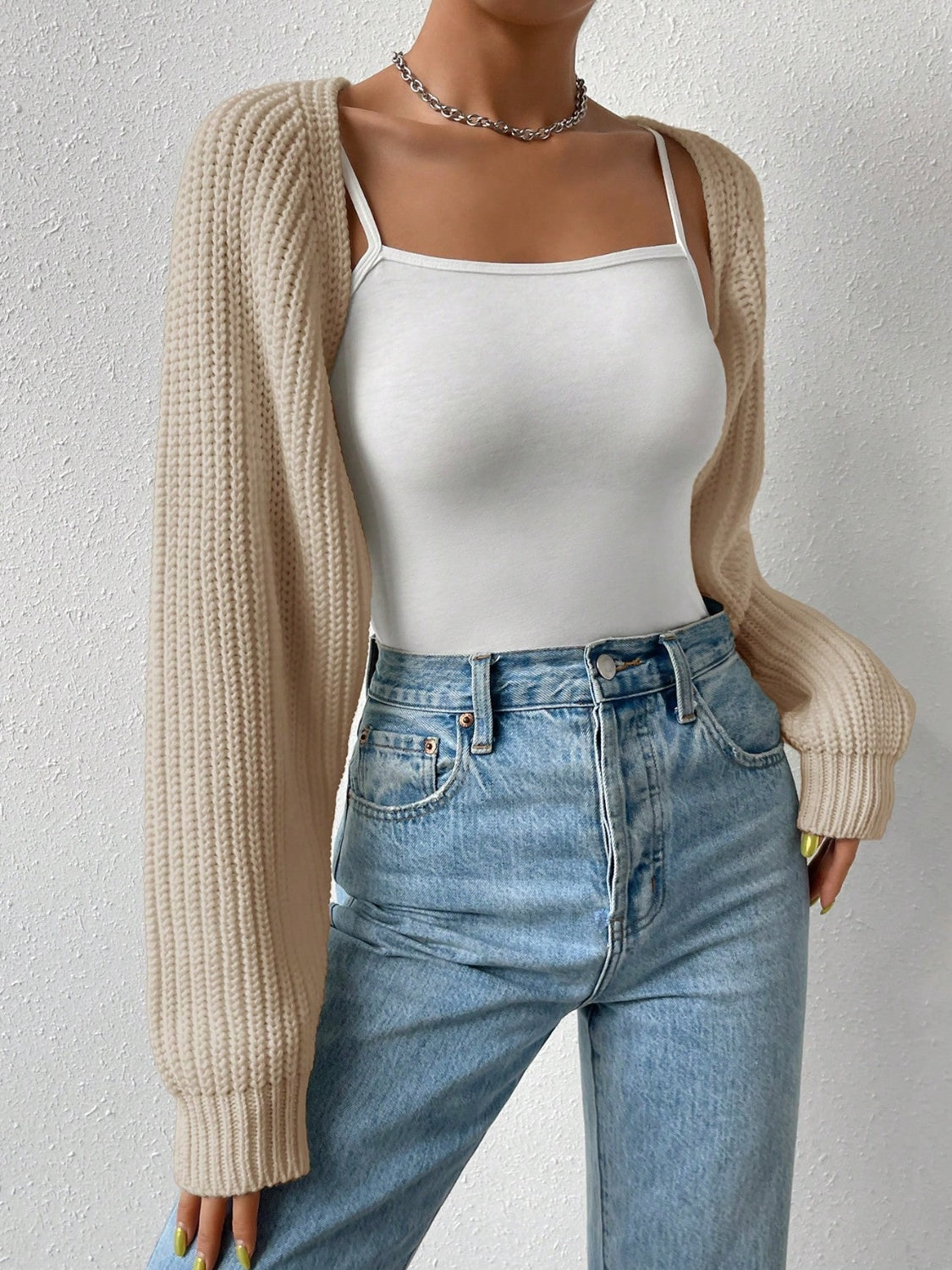 Khaki knit bolero shrug with long sleeves worn over a white cami and jeans.