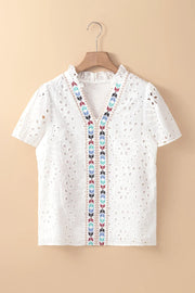 White eyelet V-neck blouse with colorful embroidered trim and ruffled collar.