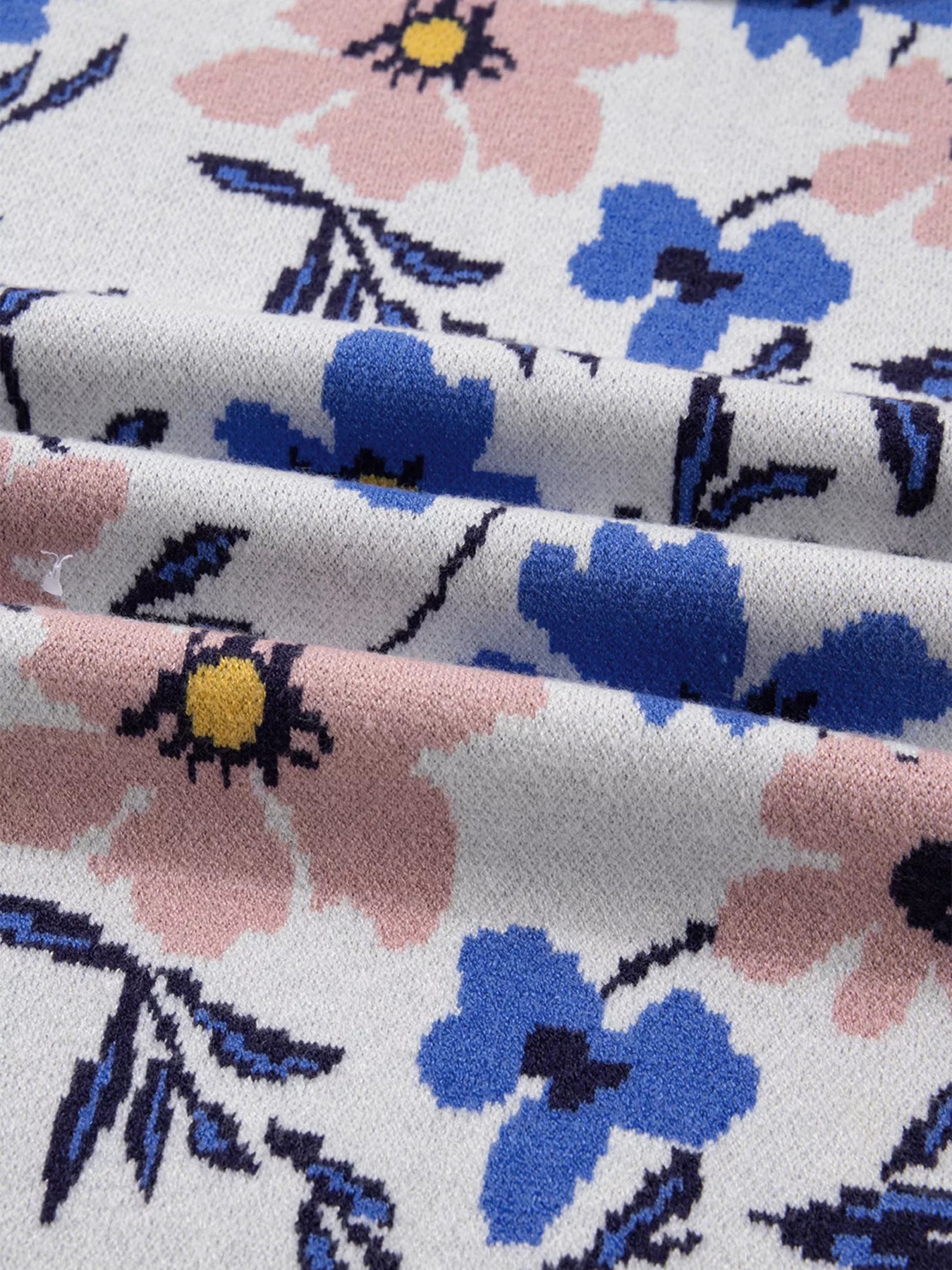 Patchwork sweater with a floral design in pink and blue on a white knit background.