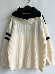 Cream ribbed knit sweater with black varsity stripes on sleeves and a black quarter-zip collar.