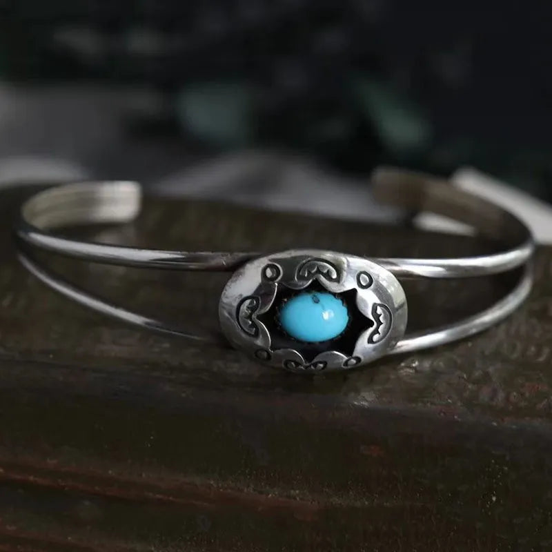 Turquoise cabochon open bangle bracelet with ornate silver setting.