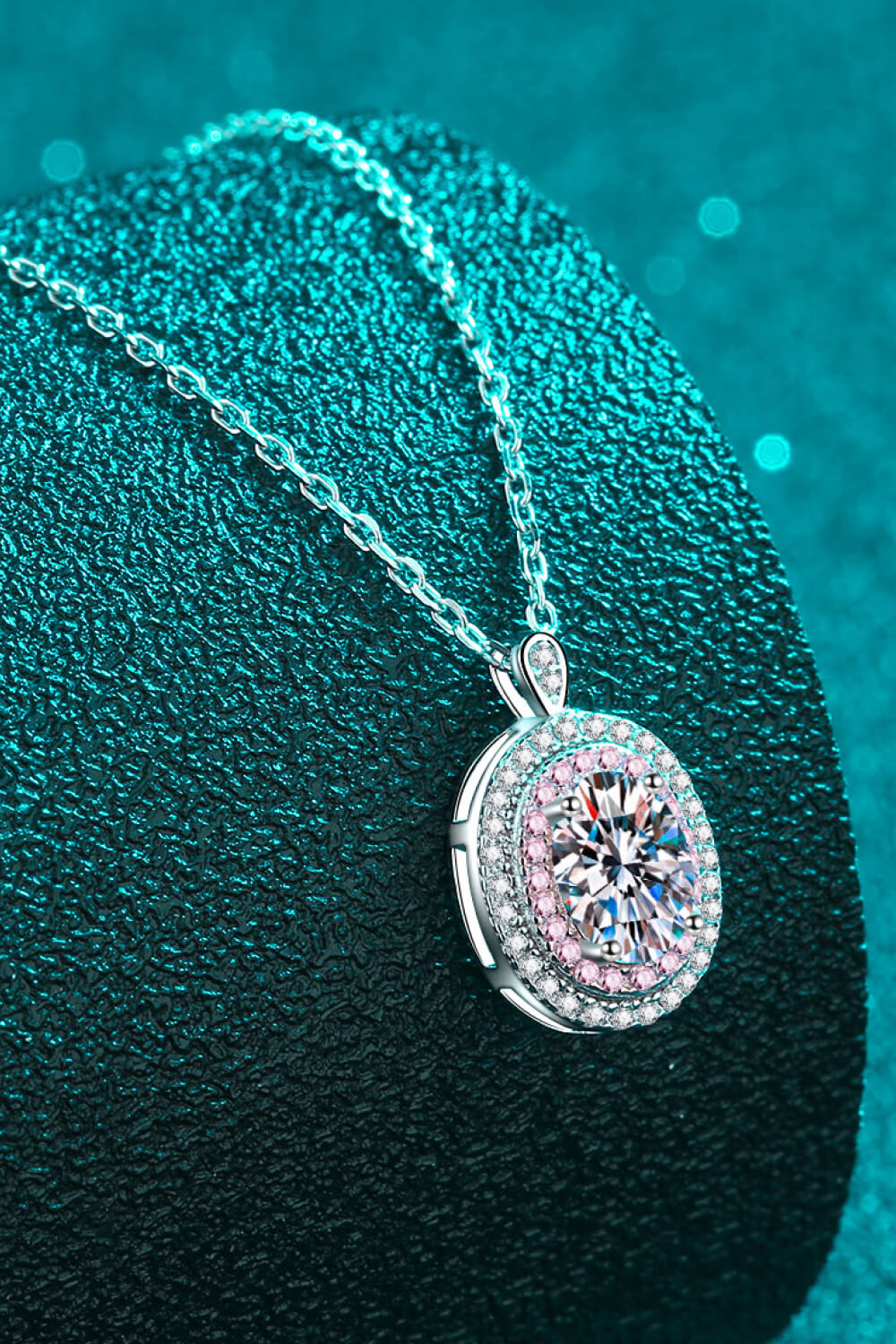 Silver halo moissanite pendant necklace with a round brilliant cut center stone and pink accent stones.