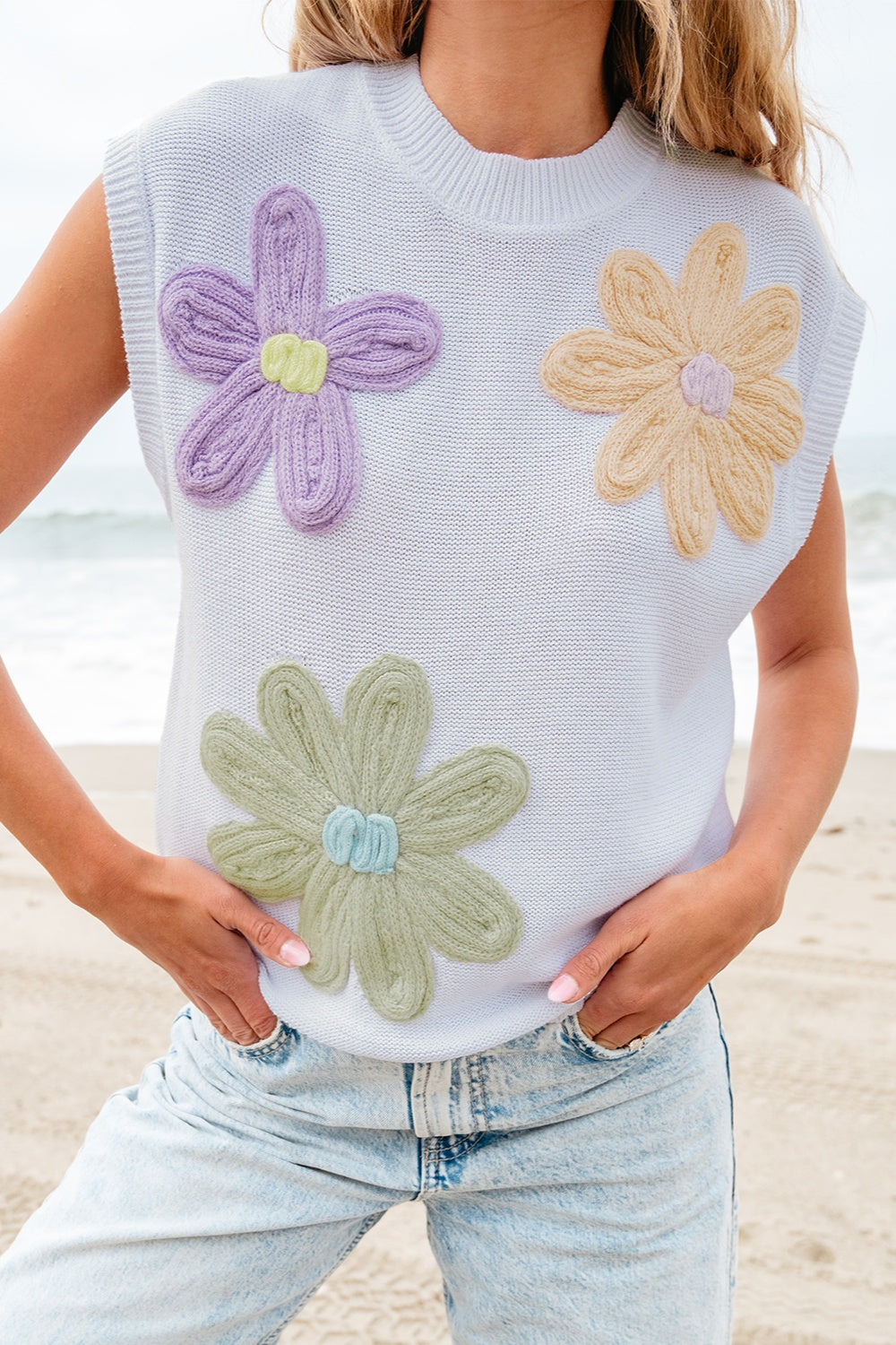 Sleeveless knit top in white with embroidered floral appliques in purple, yellow, and green.