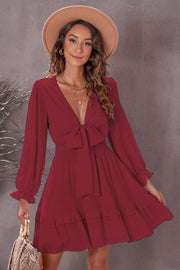 Wine ruffled mini dress with bow-tie waist, smocked bodice, and long sleeves.