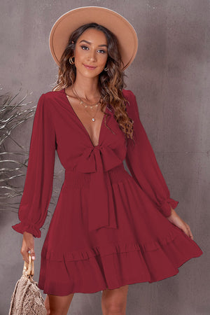 Wine ruffled mini dress with bow-tie waist, smocked bodice, and long sleeves.
