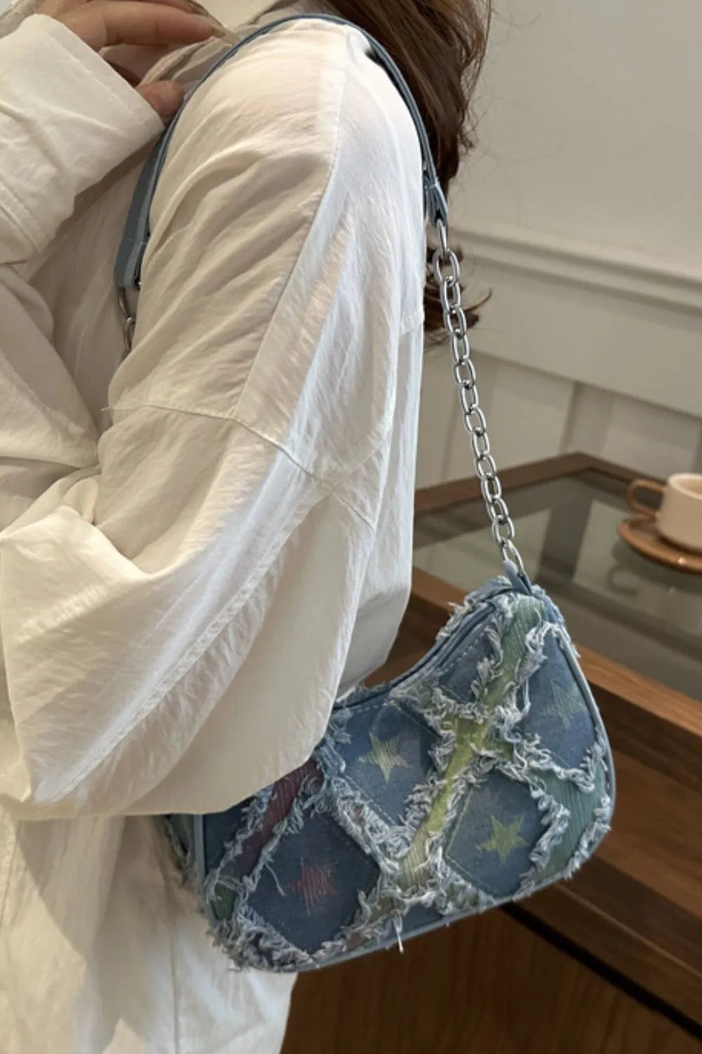 Denim shoulder bag with starburst pattern and distressed details, silver chain strap.