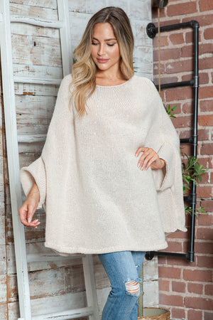 Cream knit sweater with cape sleeves and a relaxed fit, styled with ripped jeans.
