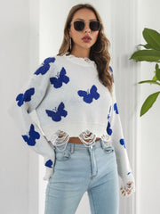 White distressed knit cropped sweater with blue butterfly print and frayed hem.