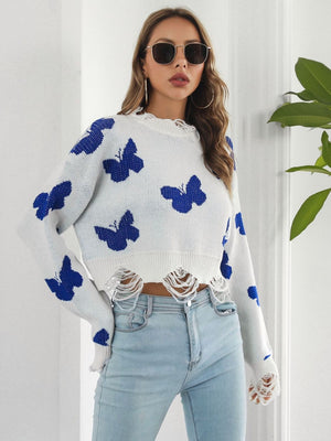 White distressed knit cropped sweater with blue butterfly print and frayed hem.