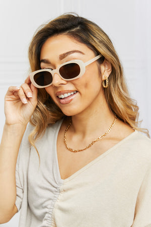 Cream tortoiseshell oval sunglasses with sunset lenses, worn by a woman with gold jewelry.
