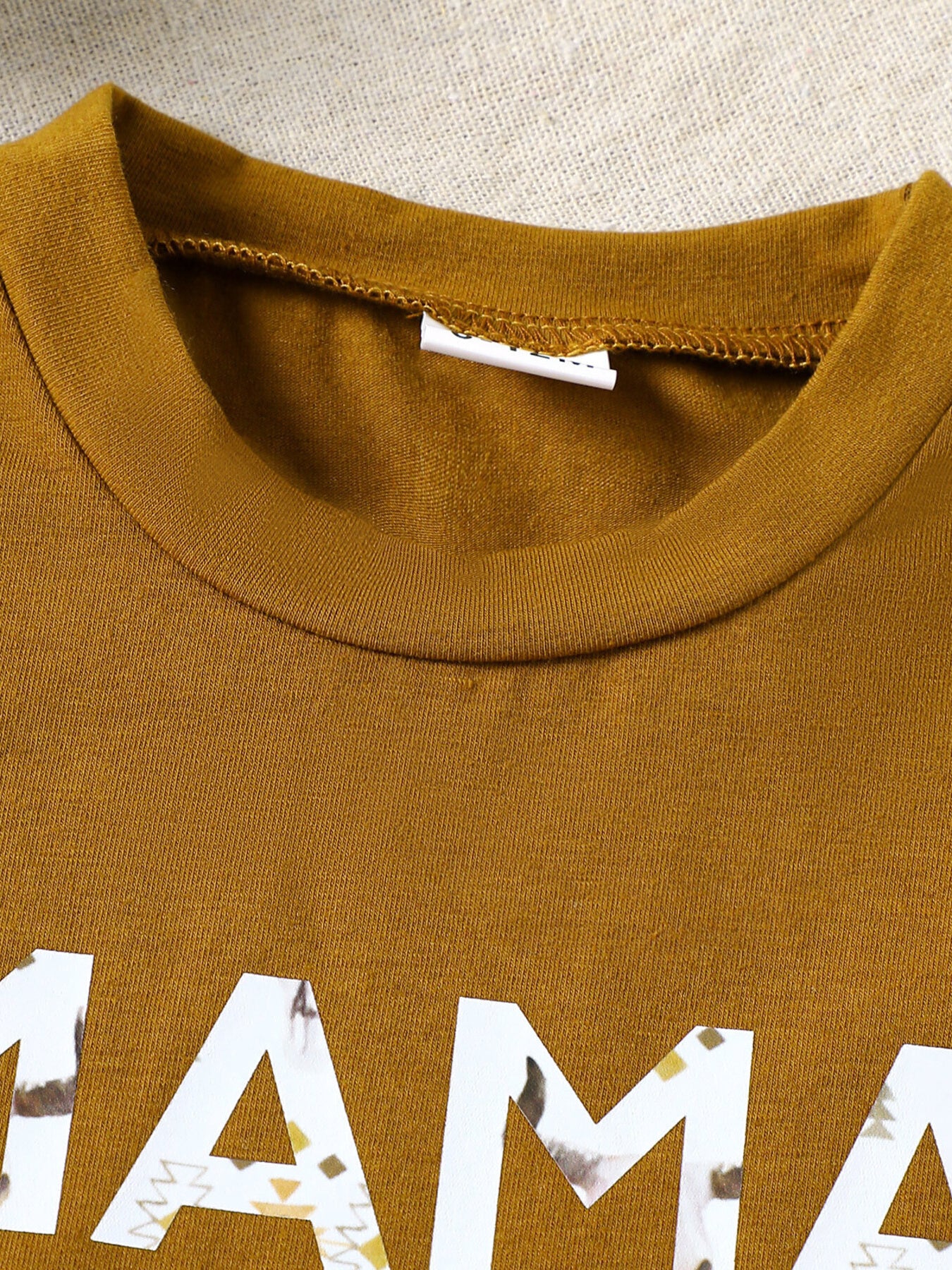 Caramel cotton blend graphic tee with "mama" text and tribal pattern detail.