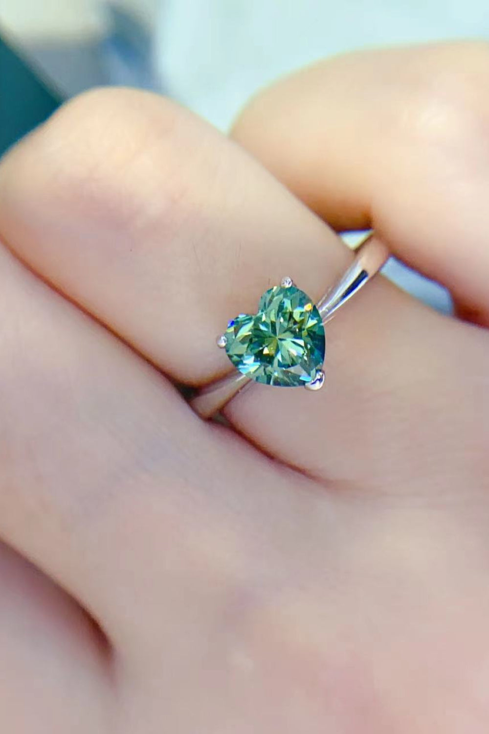 Green heart moissanite solitaire ring on a finger