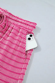 Fuchsia pink striped bikini shorts with drawstring waist and pocket holding a smartphone.