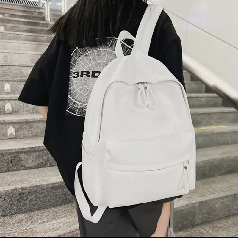White minimalist leather backpack with front pocket and double zipper closure.