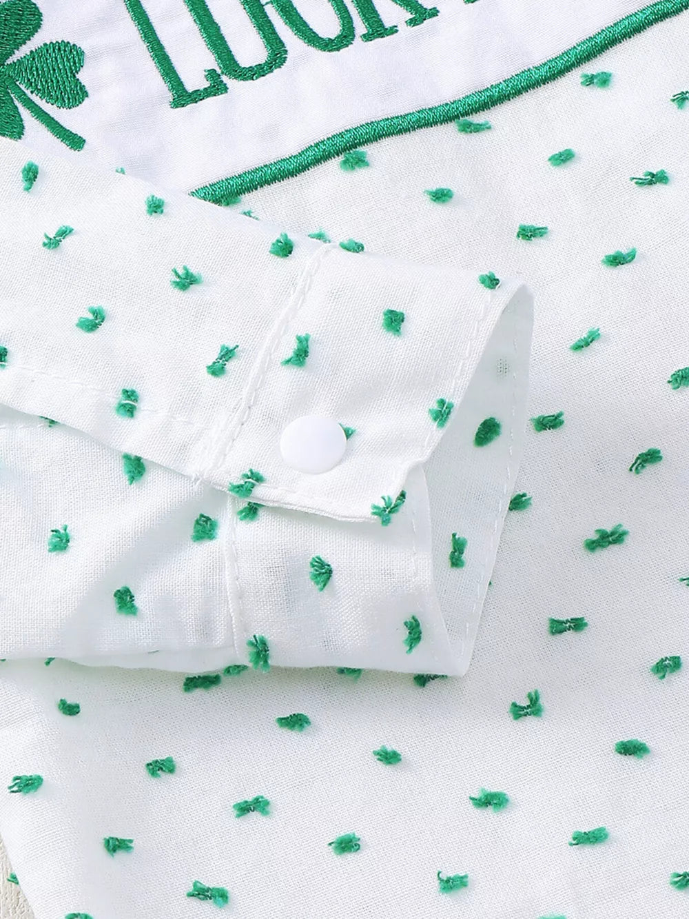 White cotton baby set with green embroidered shamrocks and text, featuring a buttoned cuff.