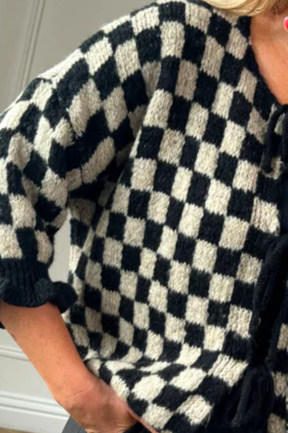 Black and cream checkered knit cardigan with ruffle sleeves and tie front detail.