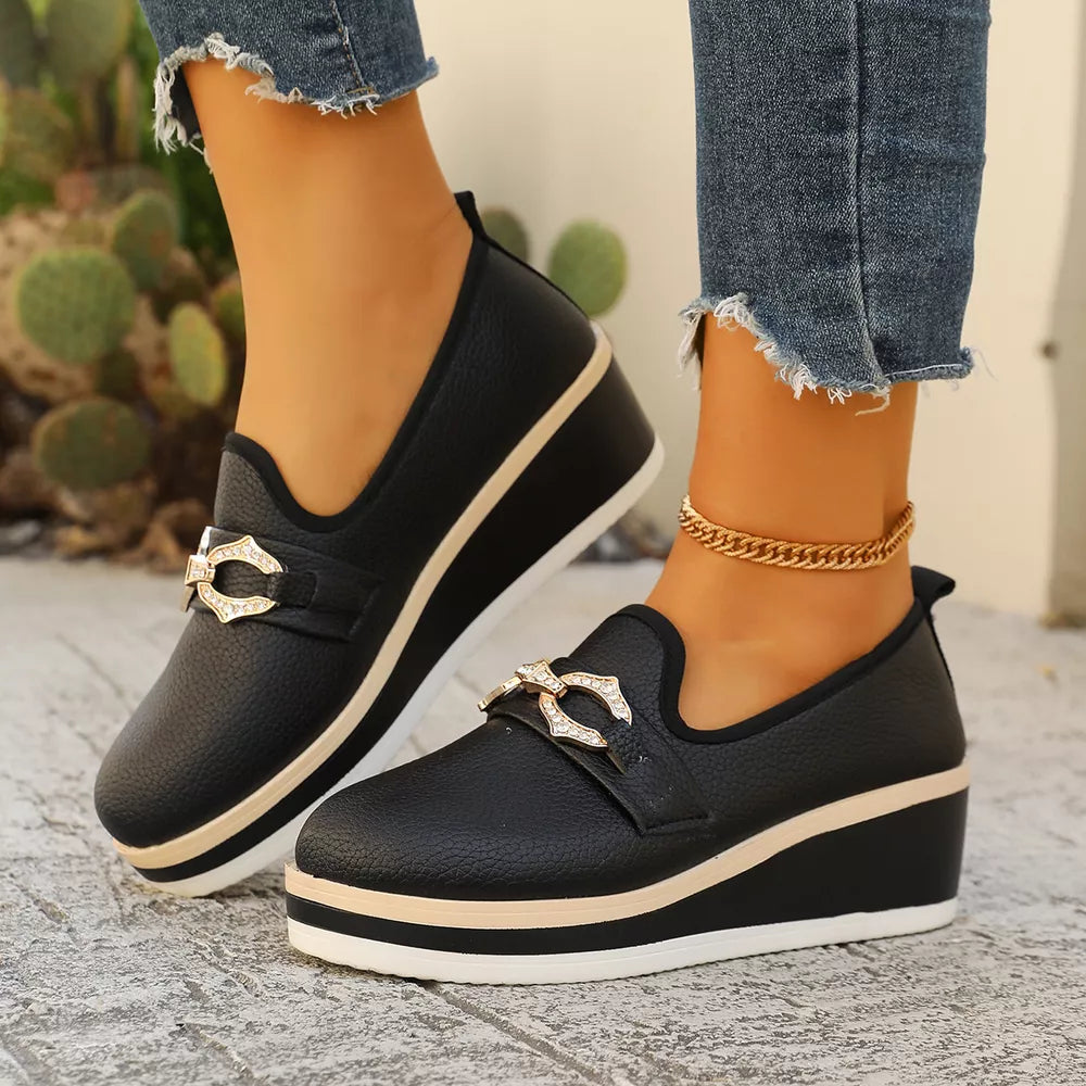 Black wedge loafers with buckle detail and layered sole.