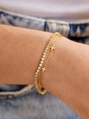 Gold chain bracelets with clear stones and cross charms on a wrist.