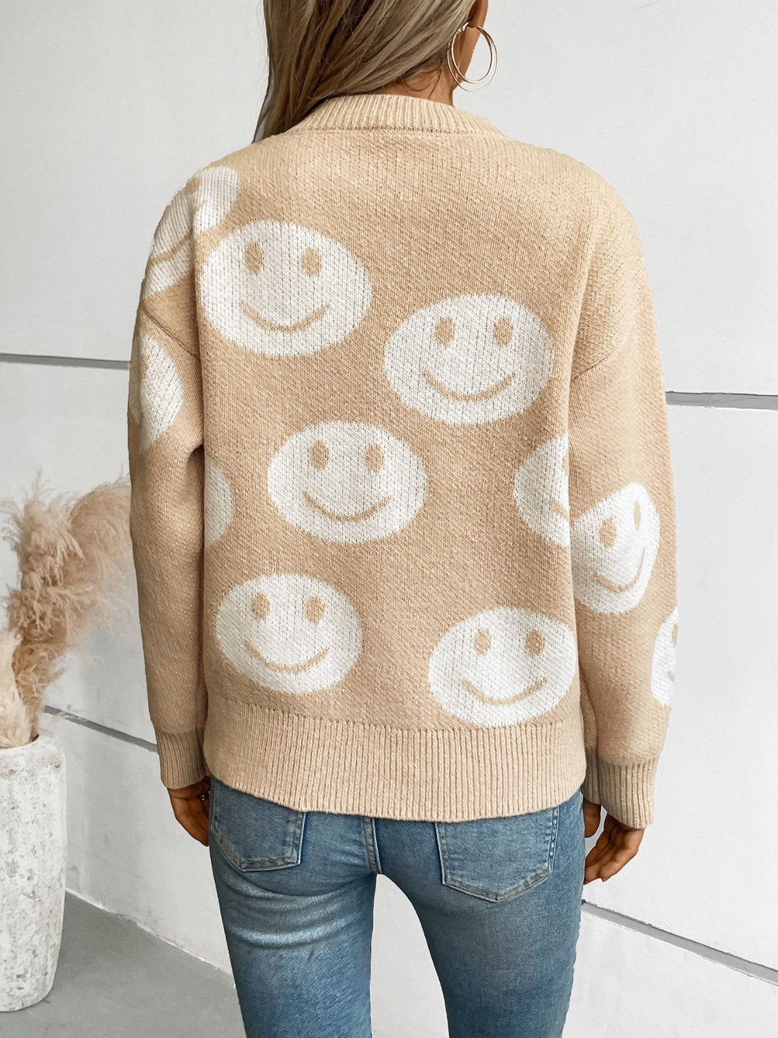 Tan intarsia knit sweater with allover white smiley faces, crew neck, and ribbed trim.