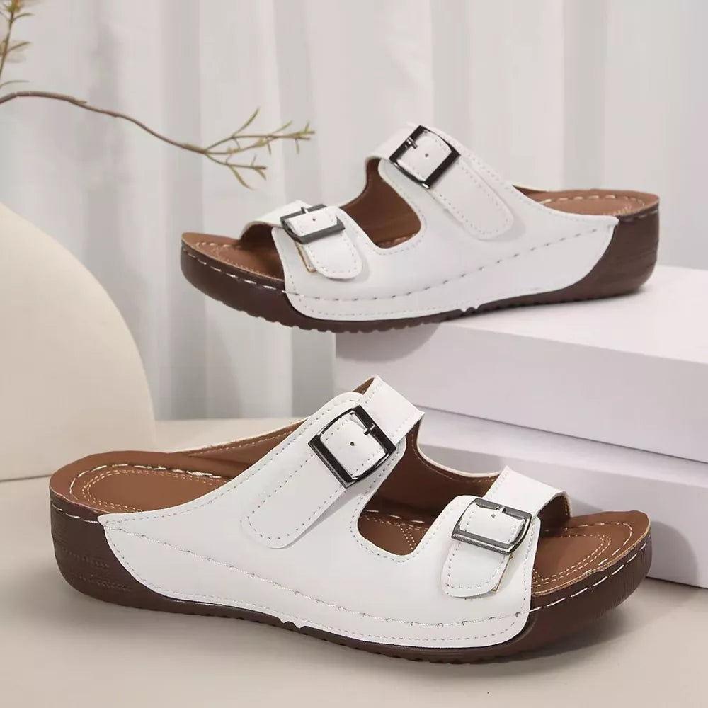White dual buckle mid-wedge sandals with adjustable straps and brown soles.