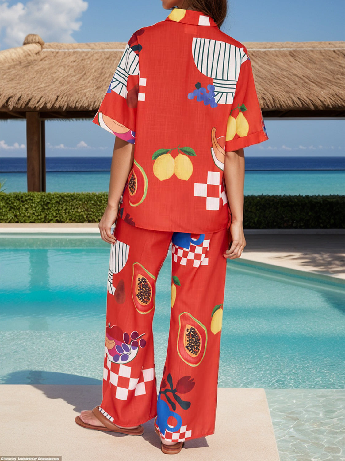 Orange-red camp shirt set with tropical fruit print, buttoned short sleeves, and wide-leg pants.