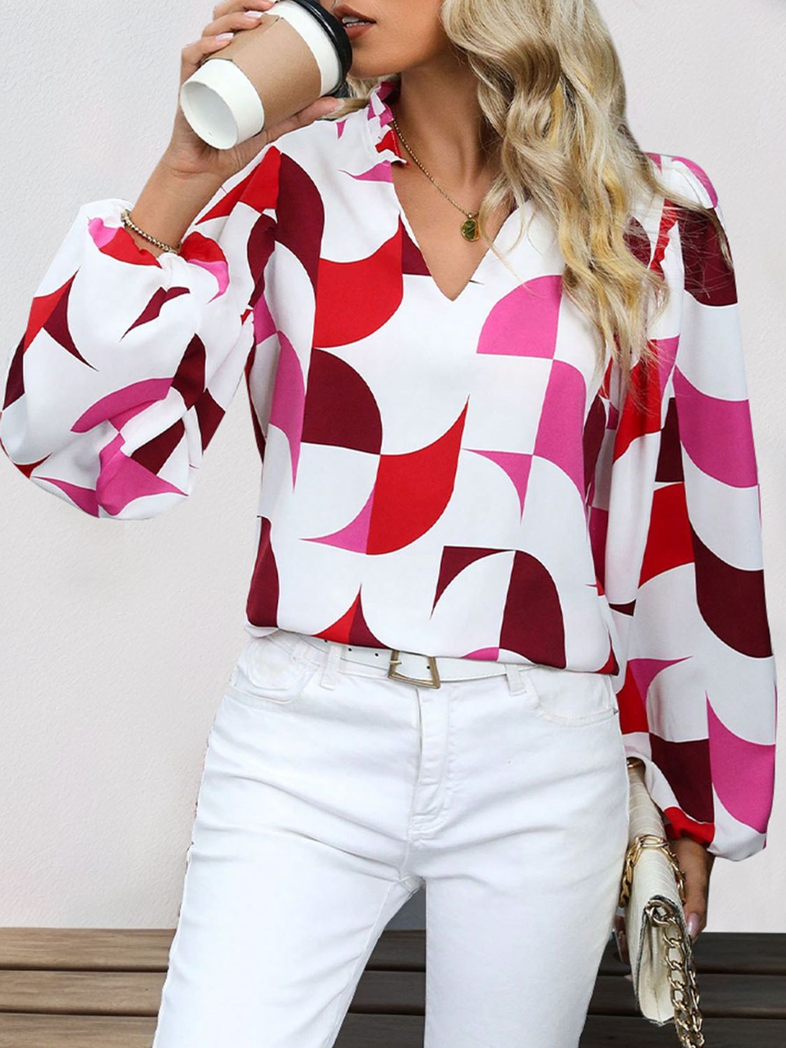 Geometric print blouse in white with pink and red shapes, featuring voluminous sleeves and a V-neck.