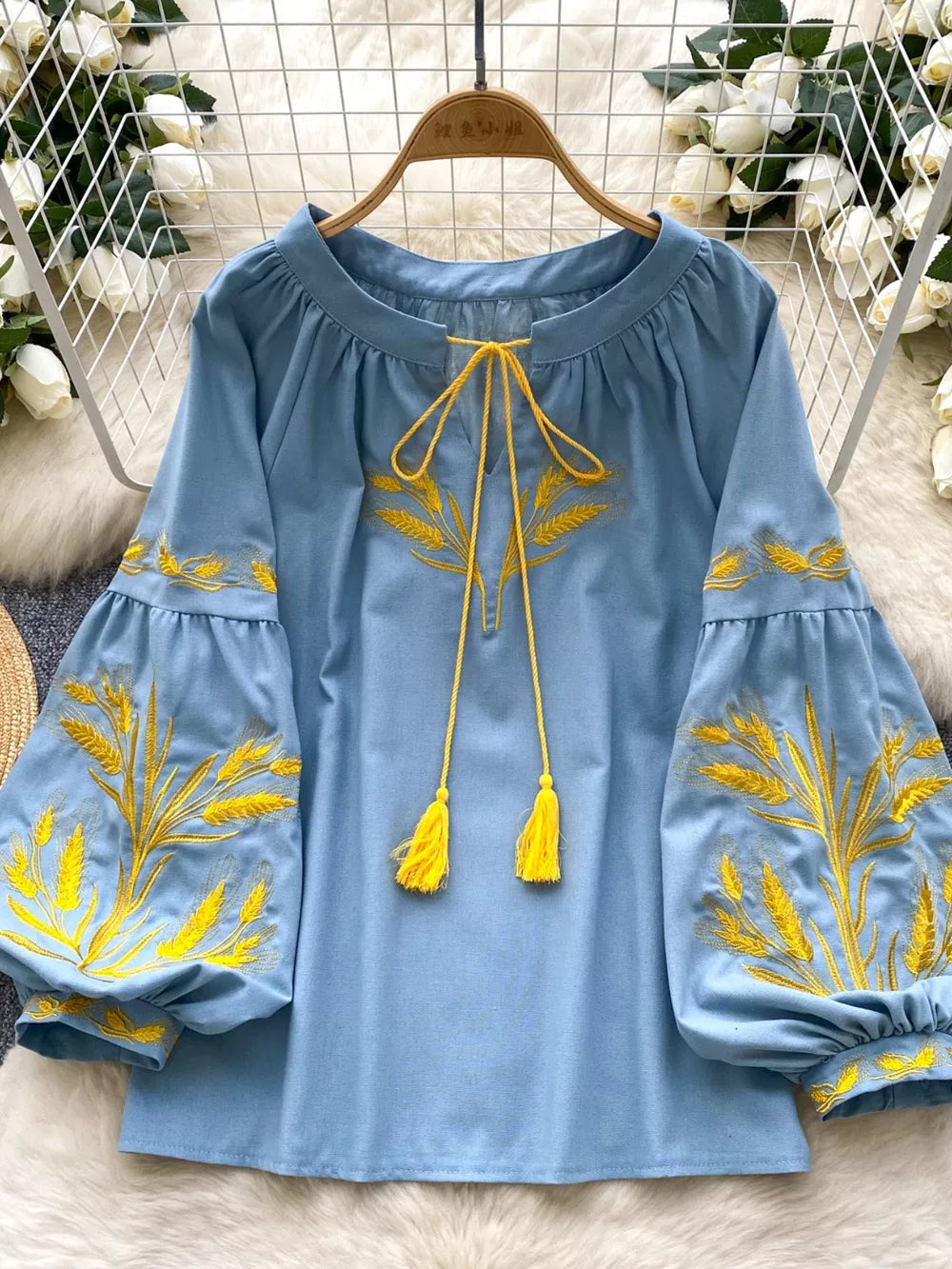 Blue tie-neck blouse with yellow wheat embroidery on sleeves and neckline, featuring tassel ties.