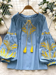 Blue tie-neck blouse with yellow wheat embroidery on sleeves and neckline, featuring tassel ties.