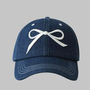 Dark blue denim baseball cap with white embroidered bow accent.