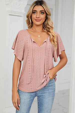 Pink eyelet tie-neck blouse with flutter sleeves and a V-neckline.
