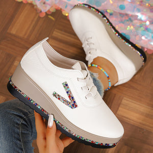 White wedge sneakers with rhinestone V detail and colorful gem trim on sole.