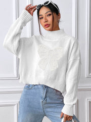 White turtleneck sweater with lace bow appliqué and ribbed trim.