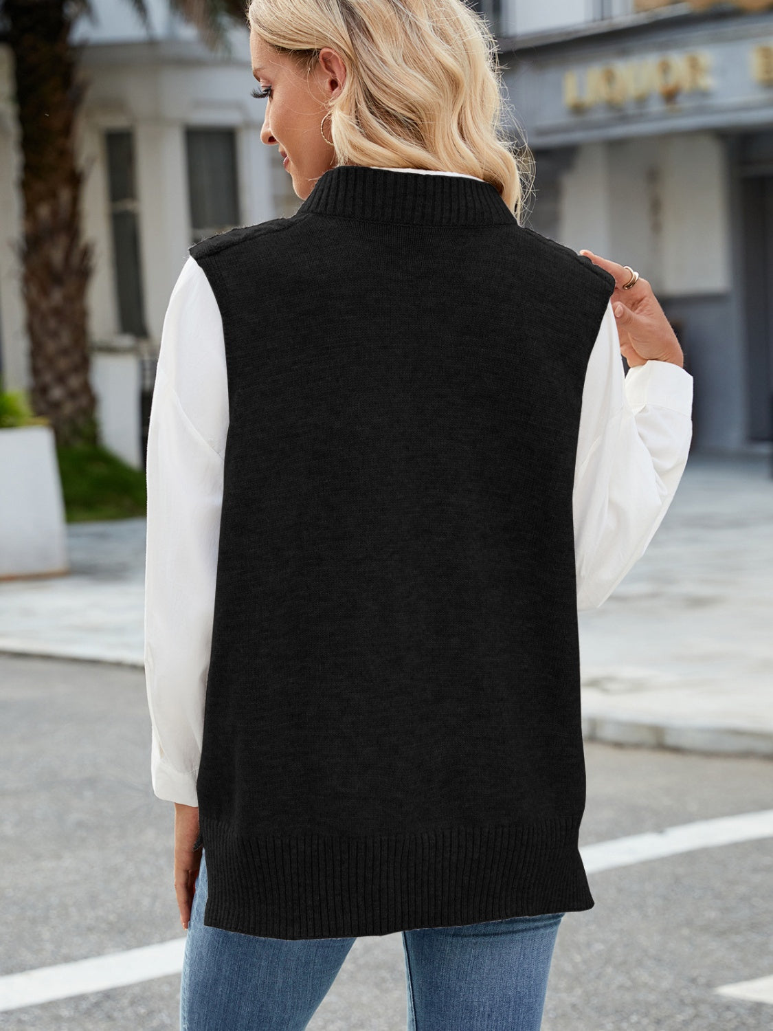 Black cable knit sweater vest with ribbed trim and mock neck, worn over a white shirt.