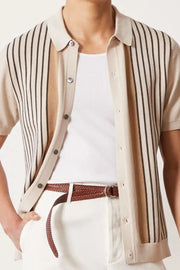 Beige knit polo shirt with vertical stripes and button front, worn over a white tank top.