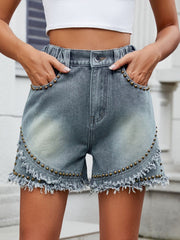Medium wash denim shorts with studded fringe detail and frayed hem